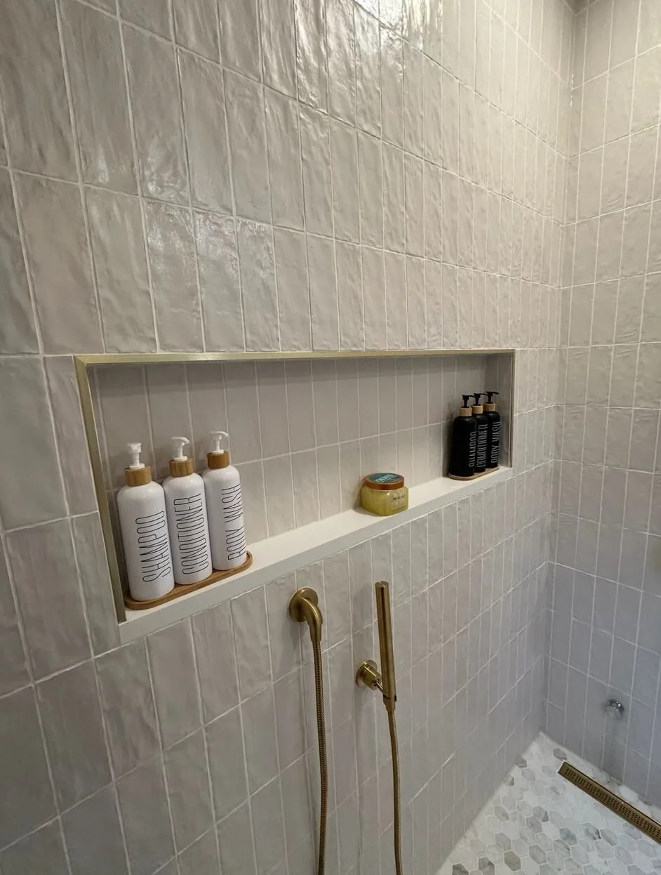 White tile shower with a long recessed niche trimmed in brass, brass shower fittings and a linear drain