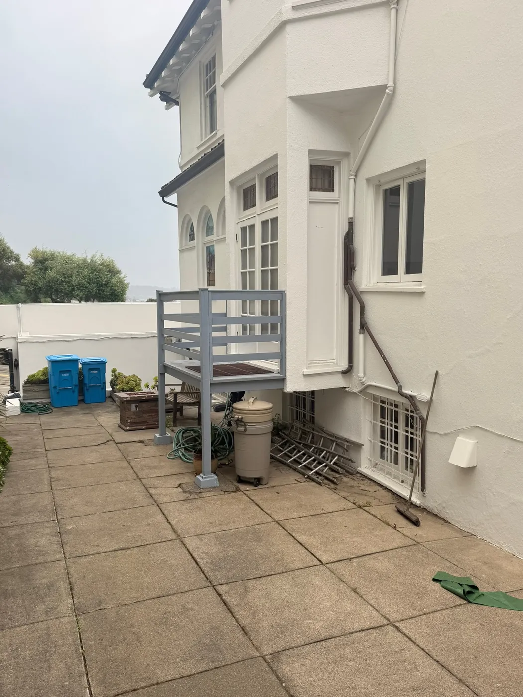 Paved patio with an old gray metal stair platform against a white stucco building