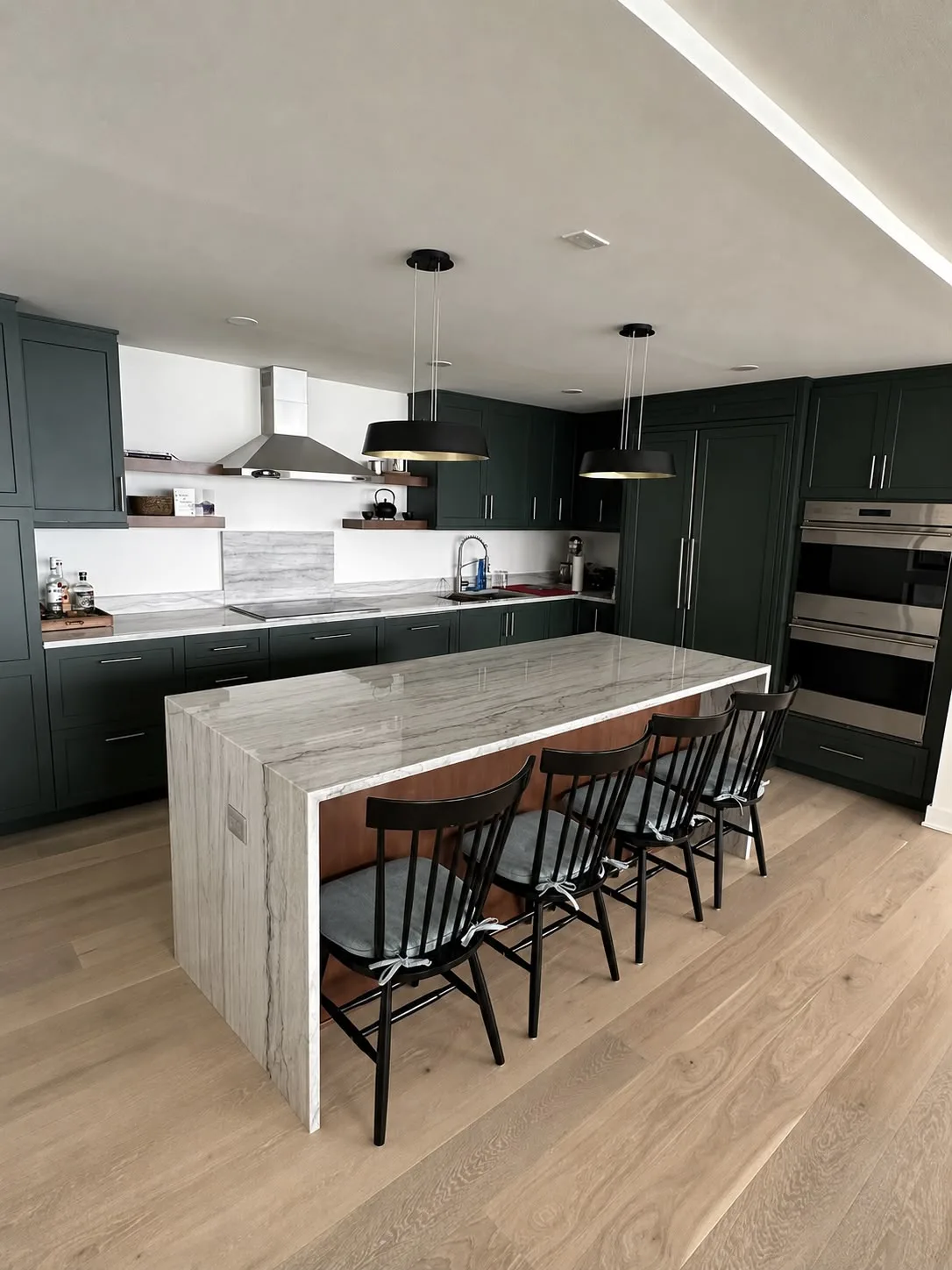 Dark green kitchen with a marble waterfall island, black pendants and oak flooring