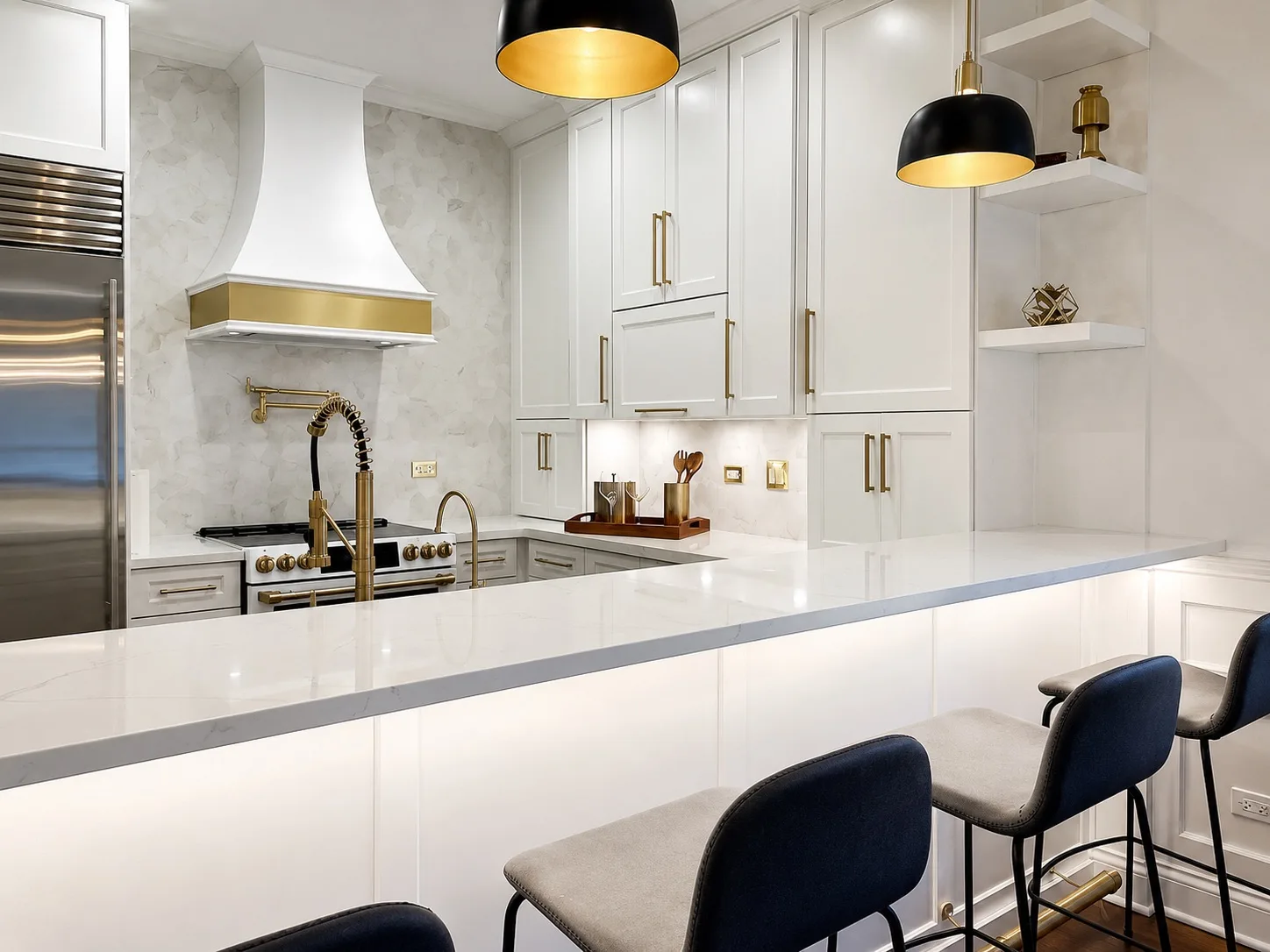 White kitchen peninsula with a quartz top and bar stools, a brass pot filler and a plaster hood banded in brass