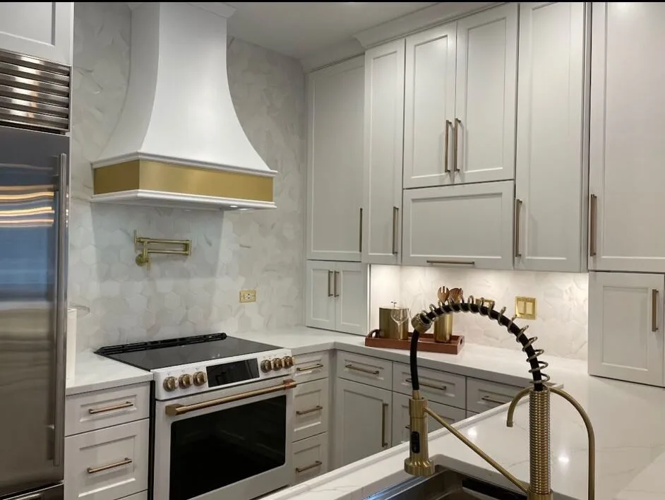 White shaker kitchen with a brass pot filler, plaster hood and marble backsplash