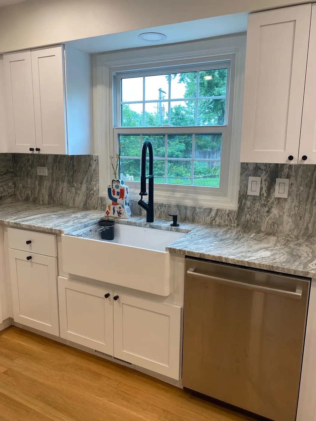 White shaker kitchen with a granite slab backsplash, farmhouse sink, black tap and stainless dishwasher