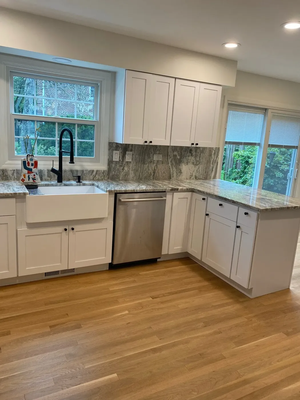 Wide view of a white shaker kitchen with stone counters, a peninsula and oak strip flooring