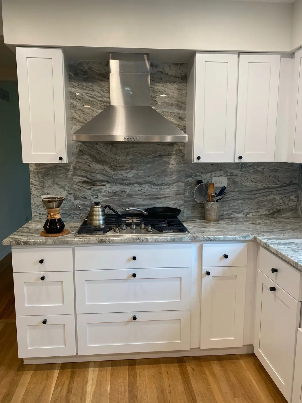 Stainless chimney hood over a gas cooktop against a full-height veined stone backsplash