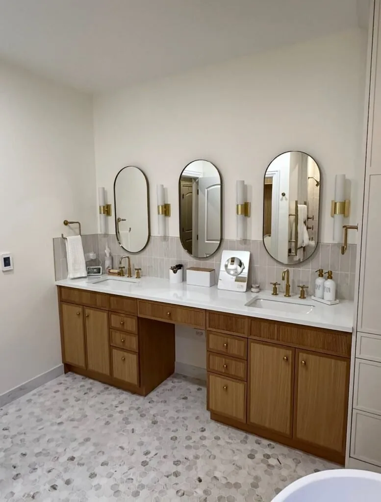 Remodeled bathroom with a wood double vanity, three oval mirrors and a walk-in shower